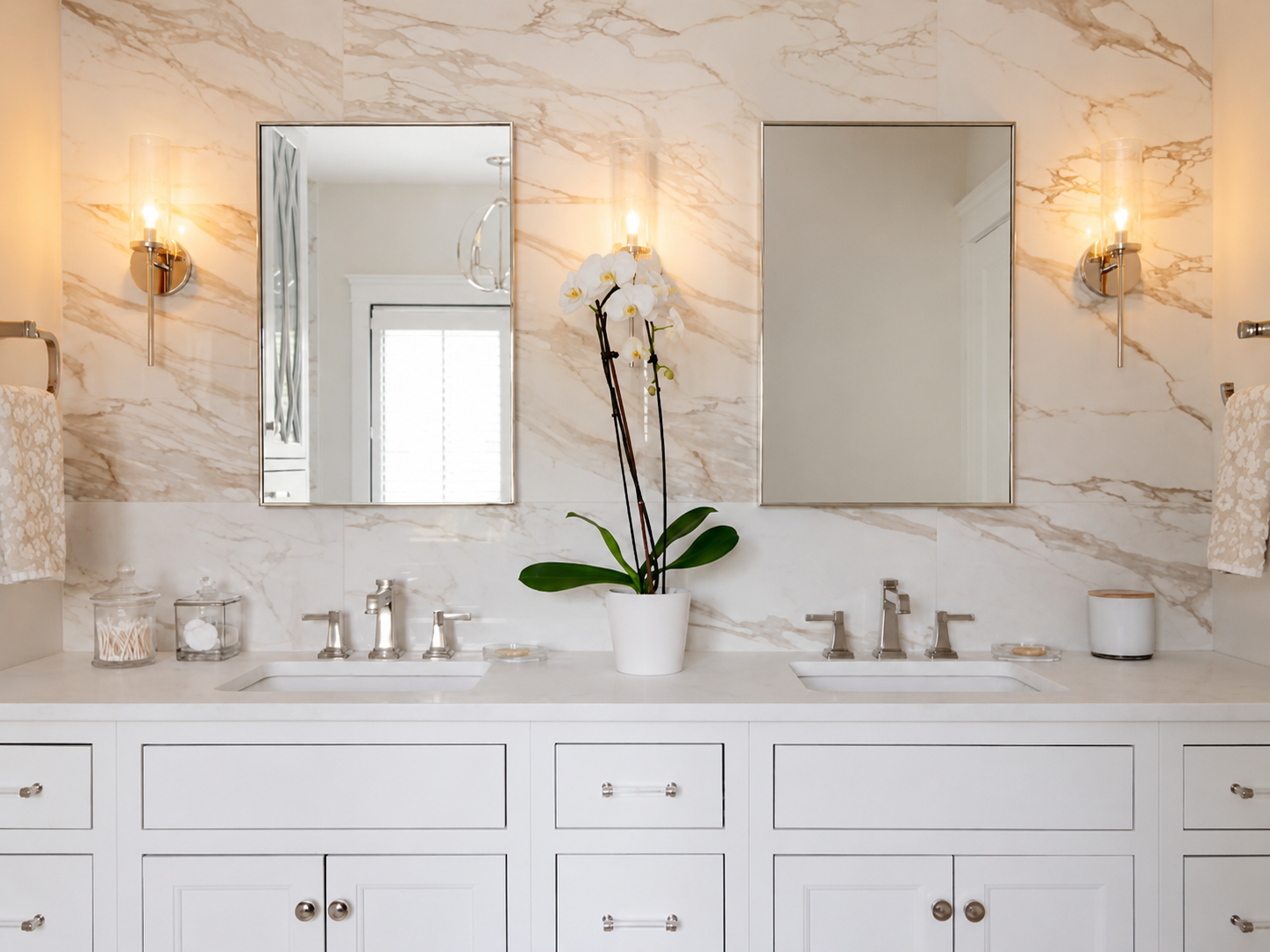 Polished nickel wall sconces flanking dual vanity mirrors against marble tile in primary bathroom at Pinehills Plymouth MA by Luster and Volt